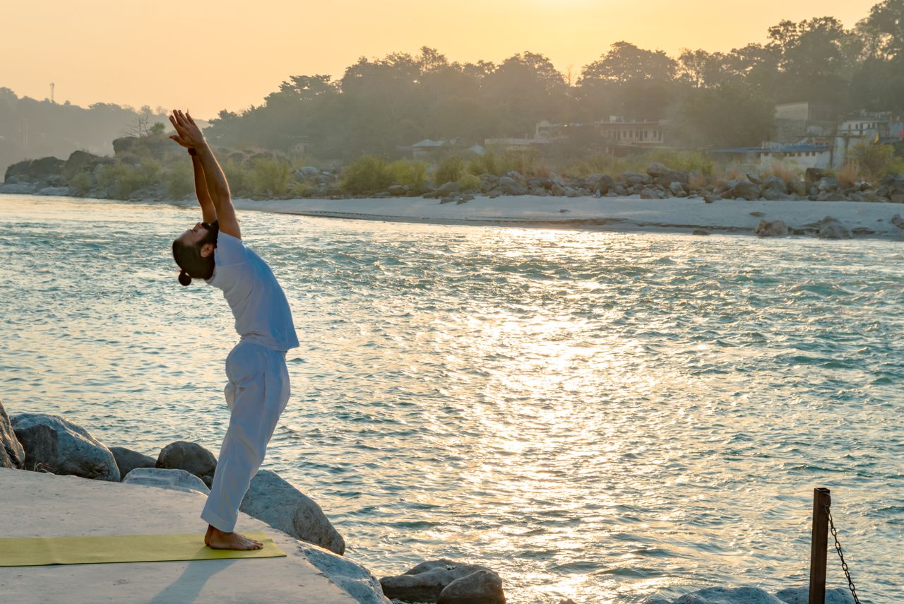 about-03 A man performs yoga by the Ganges River in Rishikesh at sunrise, embracing tranquility and mindfulness.