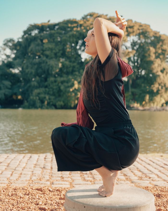 testimonial-img A woman in a yoga pose by a river in a sunny Buenos Aires park.