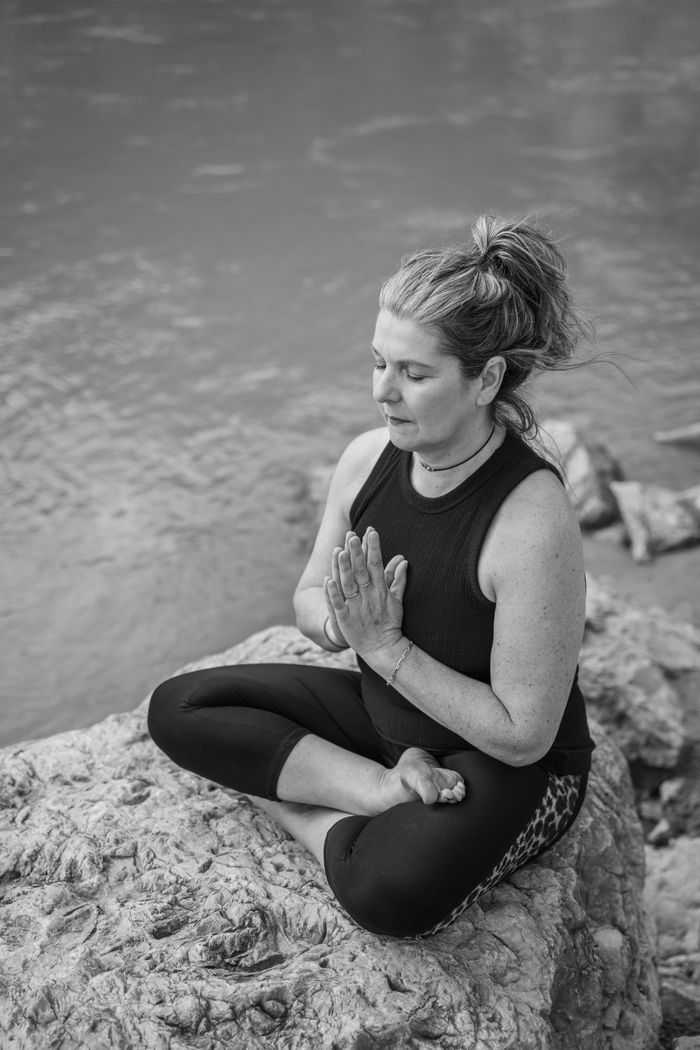 why-choose-us-01 Woman meditating on a rock by the river, displaying peaceful mindfulness and relaxation.
